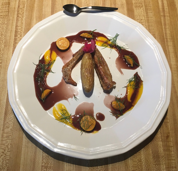 Duck wing and fingerling potato on a white plate with a spoon at the top of the plate.